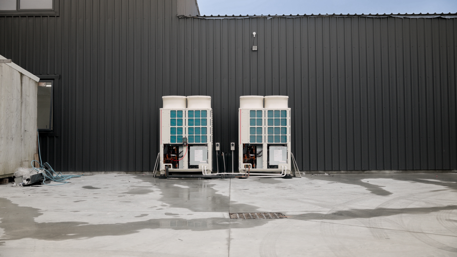 The two outdoor units against the dark profiled wall during commissioning